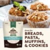 A package of Doudlah Farms' Flynn Creek Whole Wheat Flour is displayed next to muffins topped with oats and blueberries. The text reads: Perfect for Breads, Pasta, Muffins, & Cookies!