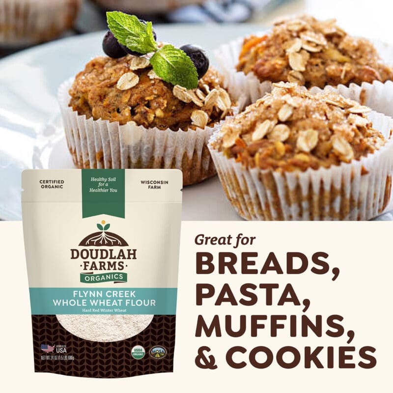 A package of Doudlah Farms' Flynn Creek Whole Wheat Flour is displayed next to muffins topped with oats and blueberries. The text reads: Perfect for Breads, Pasta, Muffins, & Cookies!