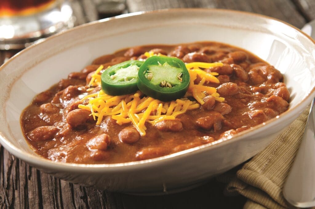 A bowl of chili infused with Latin black beans, topped with shredded cheddar cheese and sliced jalapeños, served on a rustic wooden table. The hearty dish exudes flavor and spice, embodying the essence of Latin cuisine.
