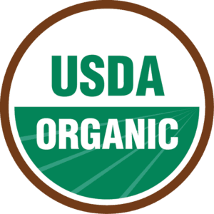 The USDA Organic logo, a circular design with a brown border, features USDA in green atop a white backdrop and ORGANIC in white on green below. We go beyond organic by showcasing the vibrancy of fields through this emblem.