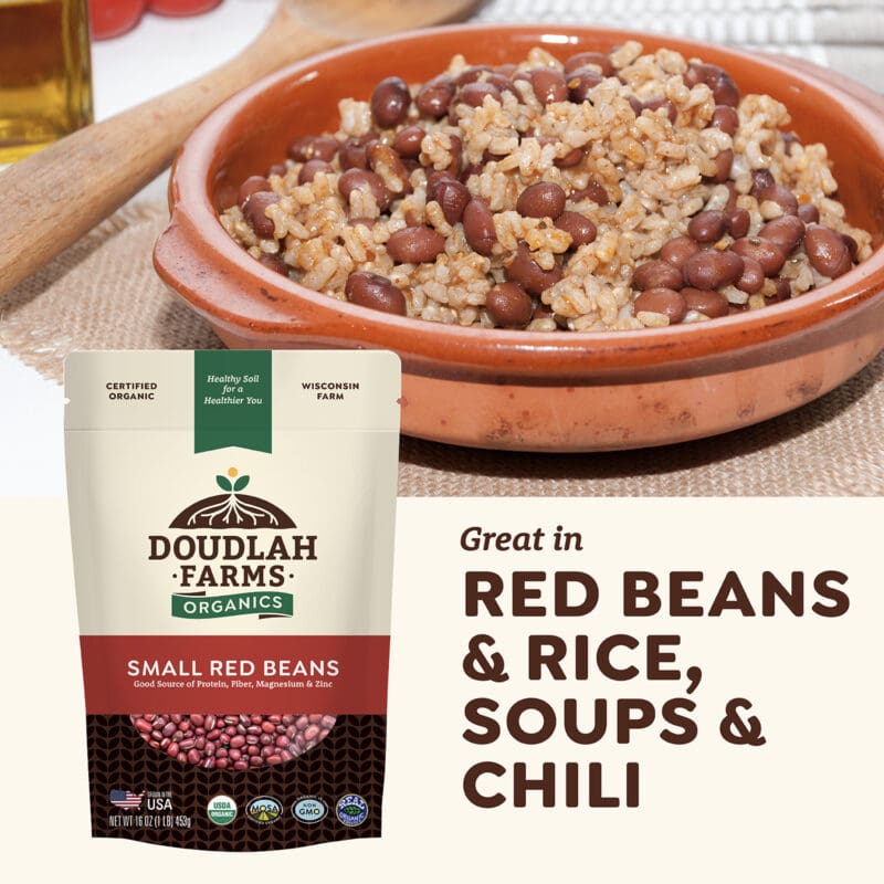 A bowl of red beans and rice is showcased alongside a package of Small Red Beans by Doudlah Farms Organics. The accompanying text highlights their suitability for red beans & rice, soups, and chili. In the backdrop, a bottle of oil and a corn cob enhance the vibrant hues of these small red gems.