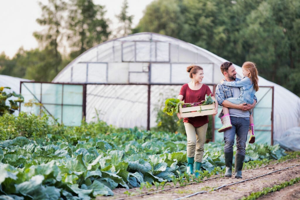 A family working on a farm with fresh vegetables and greenhouses in the background, symbolizing the role of family farms in securing a sustainable food future.