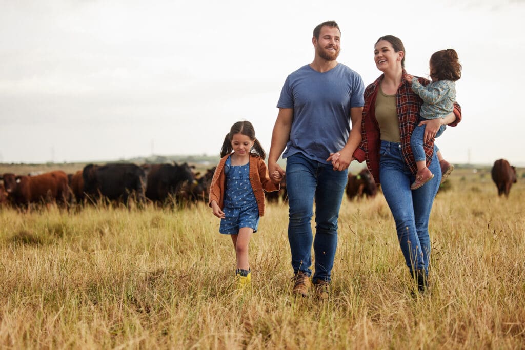 A family walking hand in hand through a pasture with cattle grazing in the background, symbolizing the connection of family farms to sustainable agriculture.