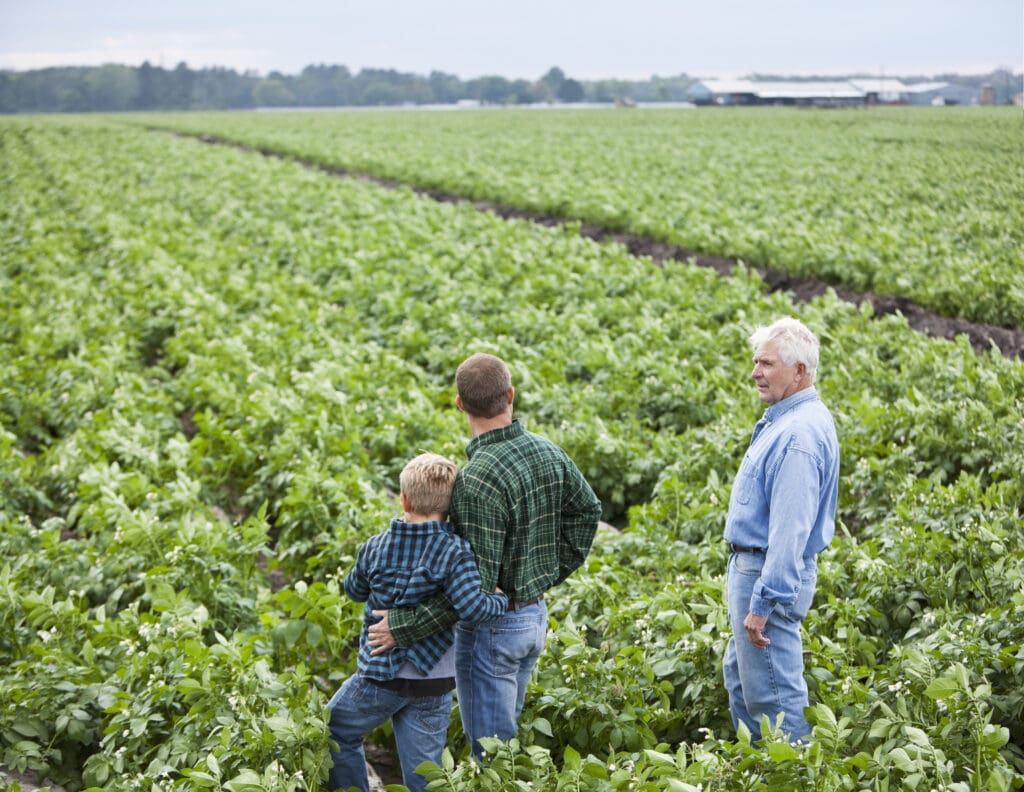 Three generations of a farming family standing in a lush green field, symbolizing the challenges and resilience of family farms in a changing world.