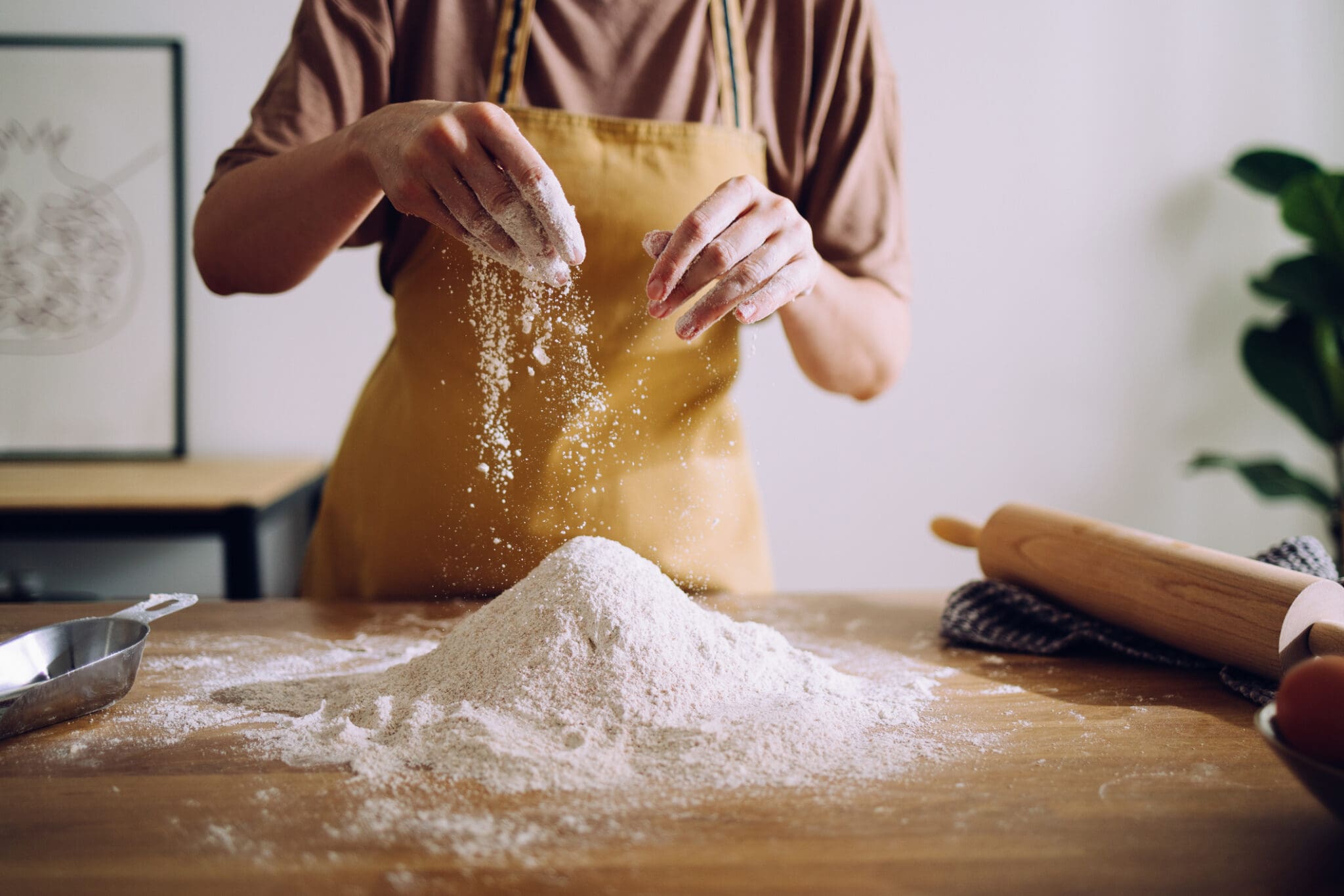 A baker sifting organic flour onto a wooden countertop, highlighting the difference between organic flour vs. conventional flour in baking and sustainability.