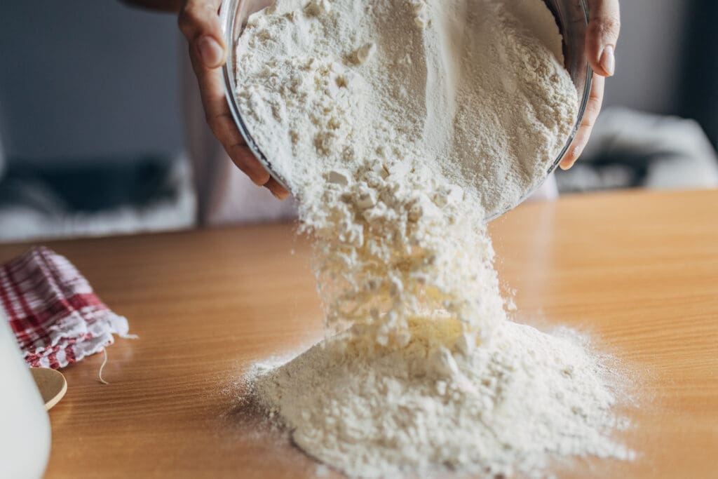 Pouring organic flour onto a wooden surface, emphasizing natural ingredients for healthy baking.