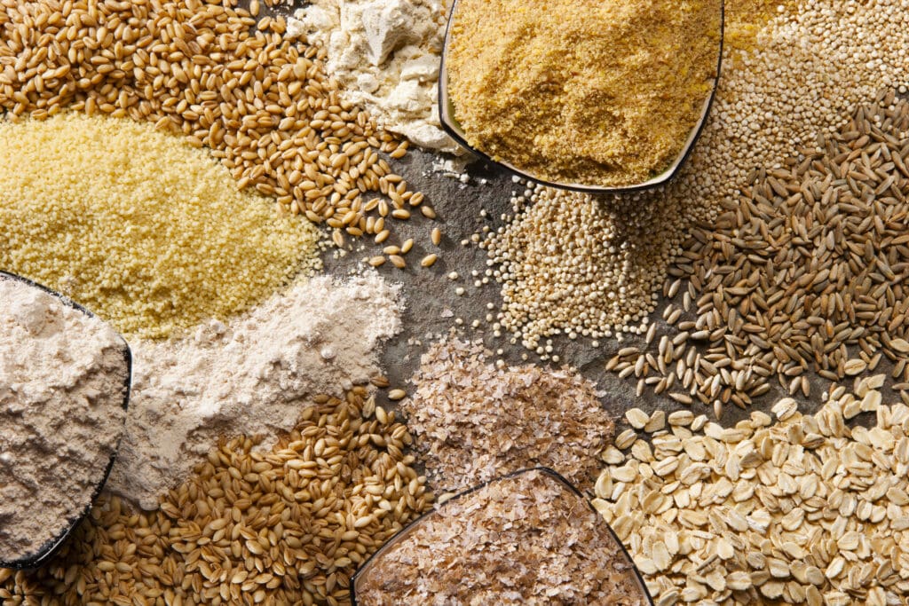 A variety of organic whole grains and flour displayed on a rustic surface, showcasing natural and unprocessed baking ingredients.