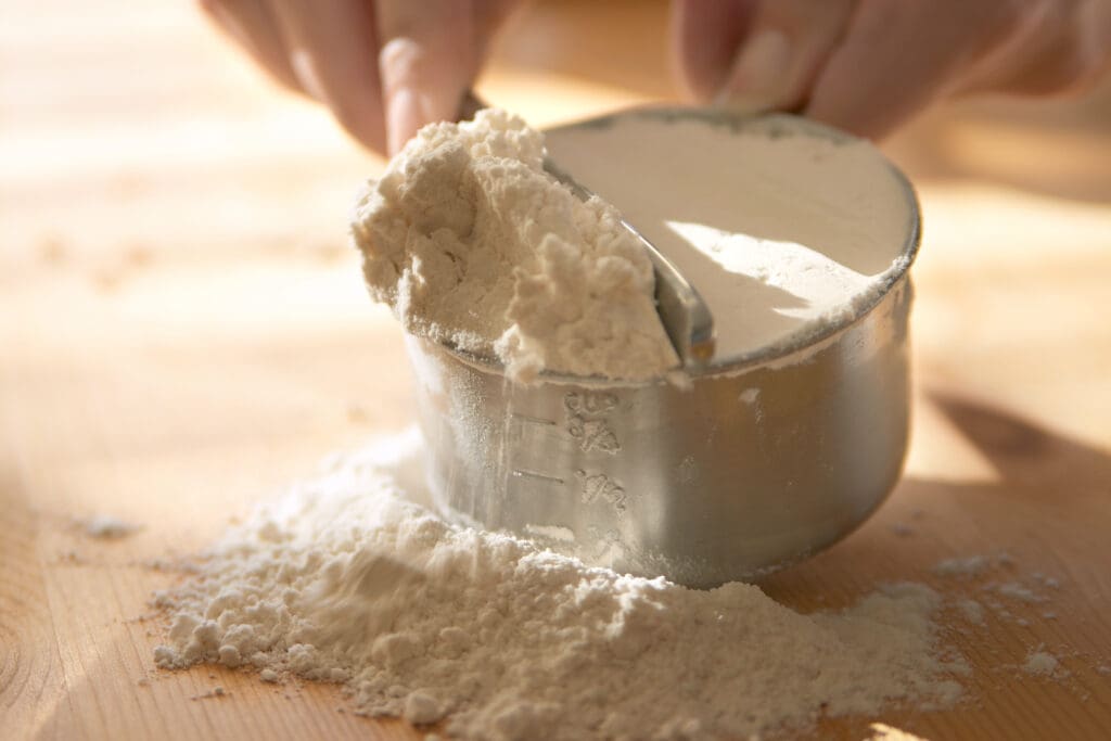 Measuring organic flour in a metal cup for baking, showcasing its natural texture and clean, chemical-free quality.
