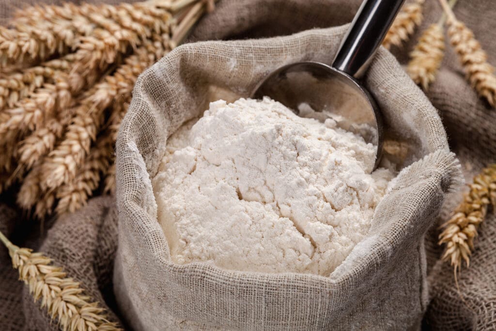 A burlap sack filled with organic flour, surrounded by golden wheat stalks, highlighting the purity and natural origins of unbleached, chemical-free flour.