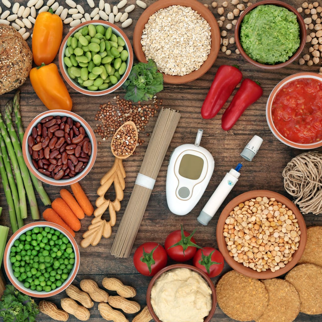 A variety of plant-based foods, including buckwheat, beans, and vegetables, arranged with a blood glucose monitor, symbolizing a diabetes-friendly diet.