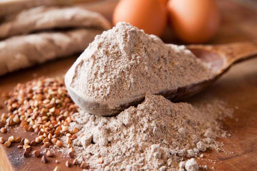 A close-up of buckwheat flour and raw buckwheat groats on a wooden surface, showcasing its gluten-free, allergy-friendly, and nutrient-rich benefits.