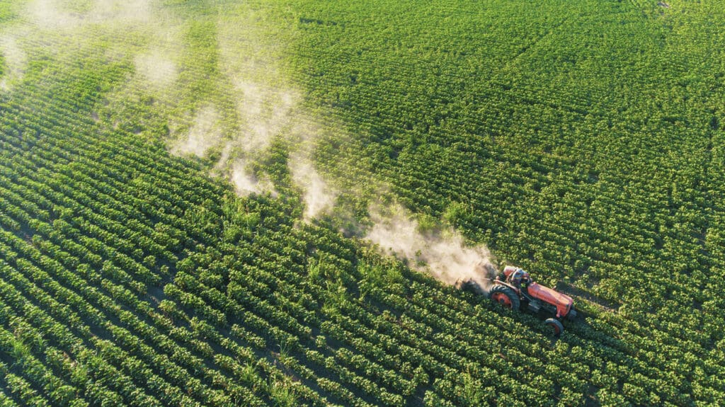 Aerial view of conventional farming with tractor spraying chemicals on crops, contrasting with organic farming environmental benefits