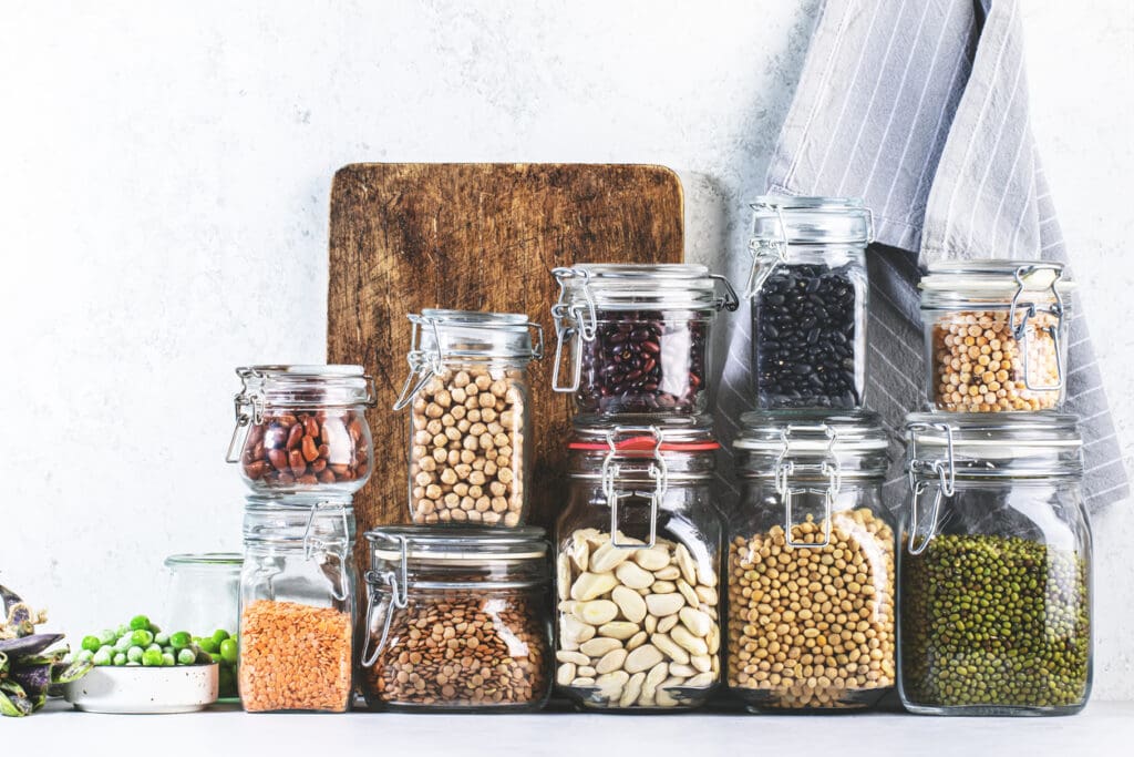 Glass jars filled with various dried beans, lentils, and legumes are arranged on a white countertop. This tidy pantry scene not only looks inviting but also supports gut health and good digestion.