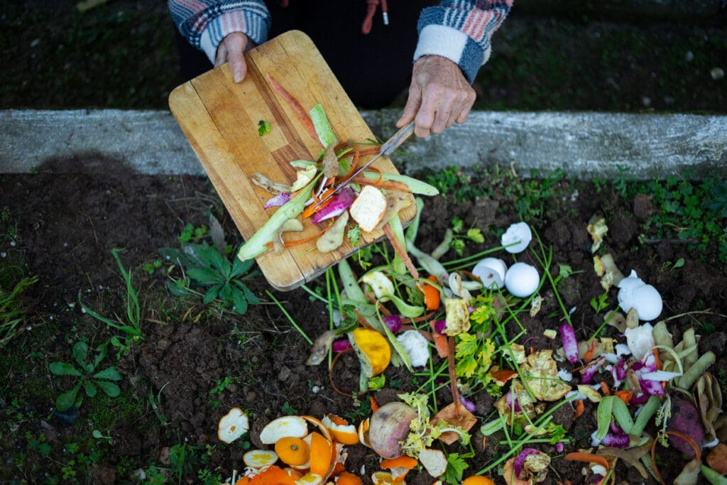 Person composting vegetable scraps and food waste into garden soil, reducing carbon footprint through sustainable organic waste management