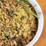 A close-up of a herb bowl of mushroom risotto featuring Emmer grain, topped with golden breadcrumbs and garnished with a sprig of rosemary, set on a wooden surface.
