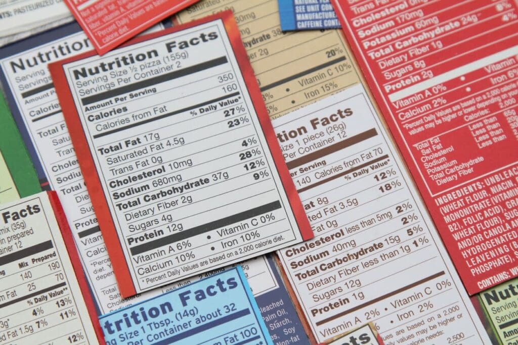 A close-up of various colorful nutrition facts labels overlapping each other, displaying information such as serving size, calories, fats, cholesterol, sodium, and other nutrients.