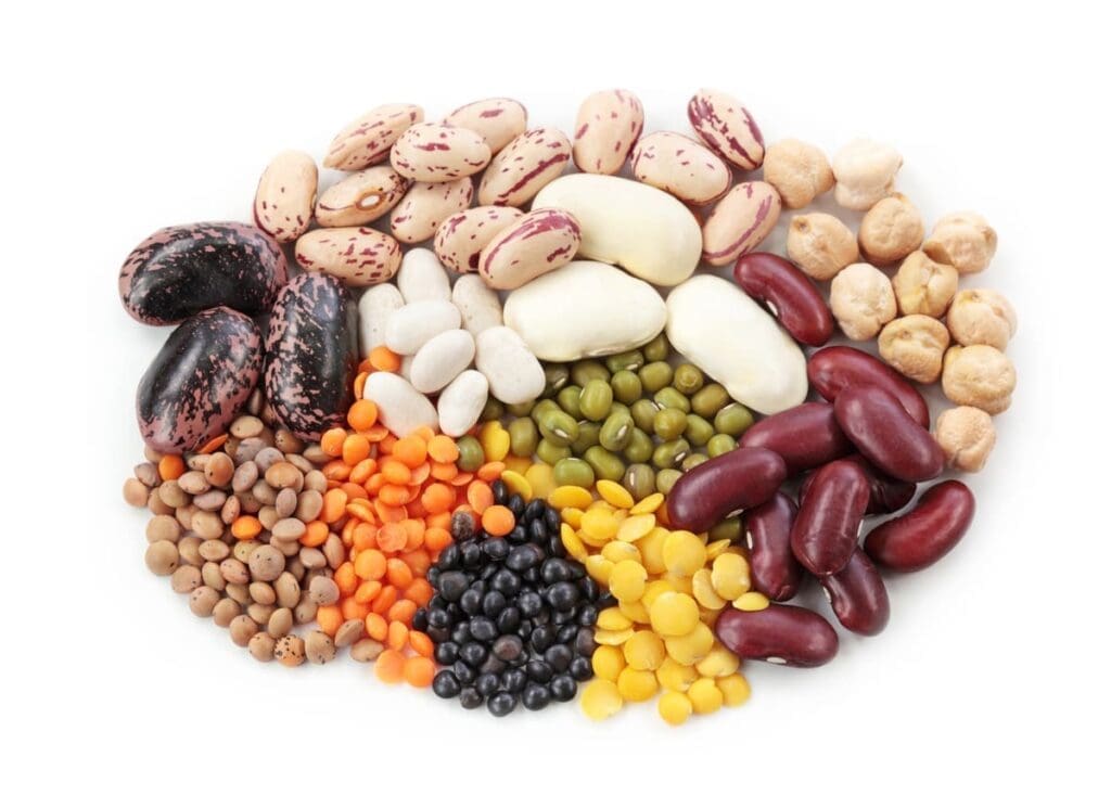 An assortment of various dried beans and lentils in different colors and shapes, arranged in a semi-circle on a white background.