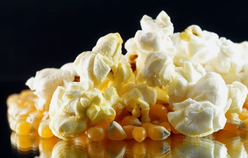 A close-up of fluffy white popcorn kernels mixed with unpopped yellow corn kernels on a glossy black surface.
