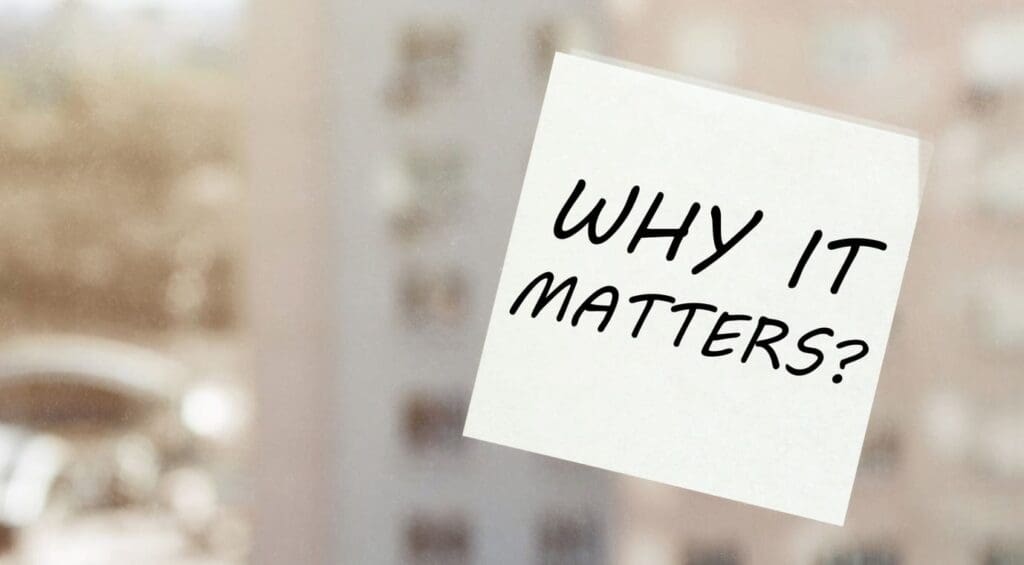 A white sticky note on a window with the handwritten message, WHY IT MATTERS? in black ink. The background is blurred, showing an urban or cityscape view.
