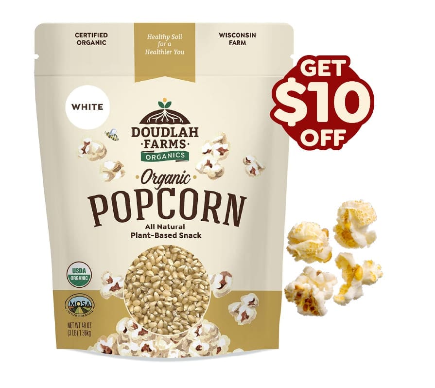 A bag of Doudlah Farms Organics white organic popcorn, with popped all-natural popcorn scattered nearby and a red Get $10 Off label on the upper right. The packaging highlights it as USDA organic and plant-based.