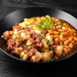 Plate of corned beef and potato hash served next to pinto beans in tomato sauce.