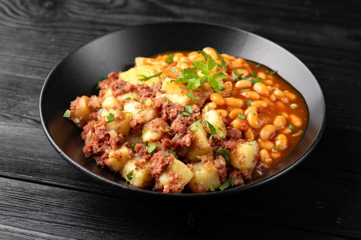 Plate of corned beef and potato hash served next to pinto beans in tomato sauce.