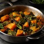 Stainless steel skillet filled with cooked butternut squash, kale, and pink beans.