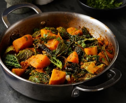 Stainless steel skillet filled with cooked butternut squash, kale, and pink beans.