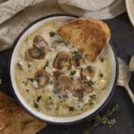 Bowl of creamy white bean mushroom soup topped with sliced mushrooms and fresh thyme, served with toasted bread.