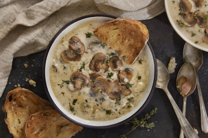 Bowl of creamy white bean mushroom soup topped with sliced mushrooms and fresh thyme, served with toasted bread.